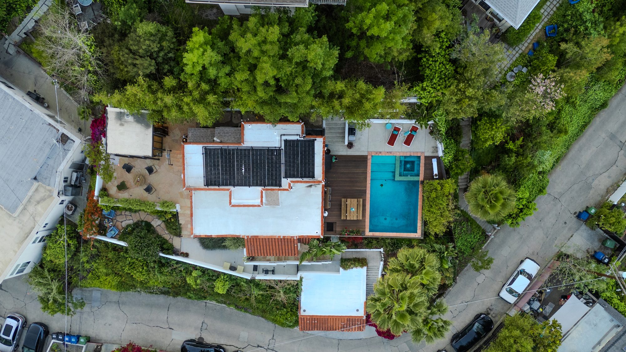 Straight-down aerial view of the terraced lot: the house with rooftop solar panels in the center, pool and deck to the north, studio and stone terrace to the south, garage at the street