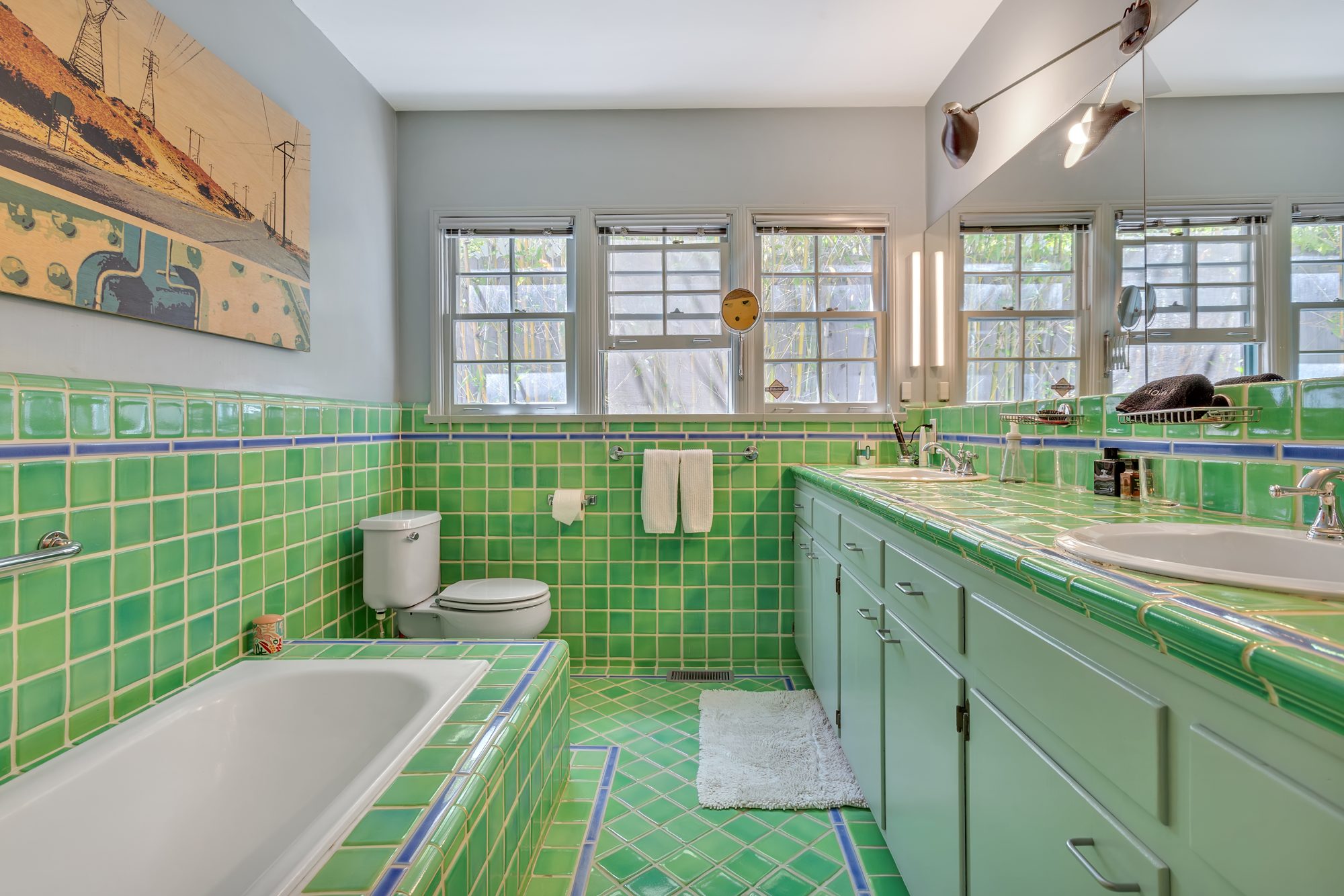 Bathroom in original green ceramic tile with a cobalt accent stripe, tub, double sink counter, and a row of windows