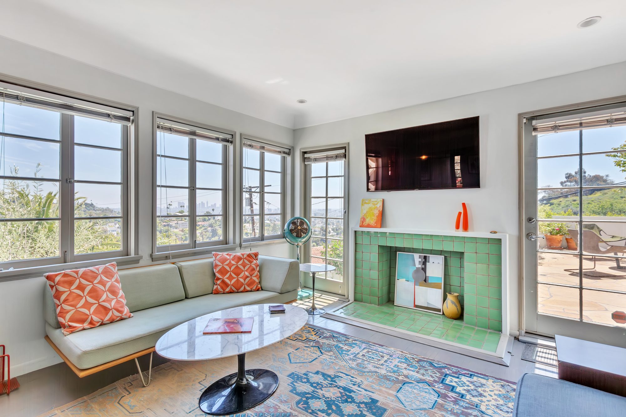 Living room with wood casement windows framing the city view, and a fireplace faced in original green ceramic tile