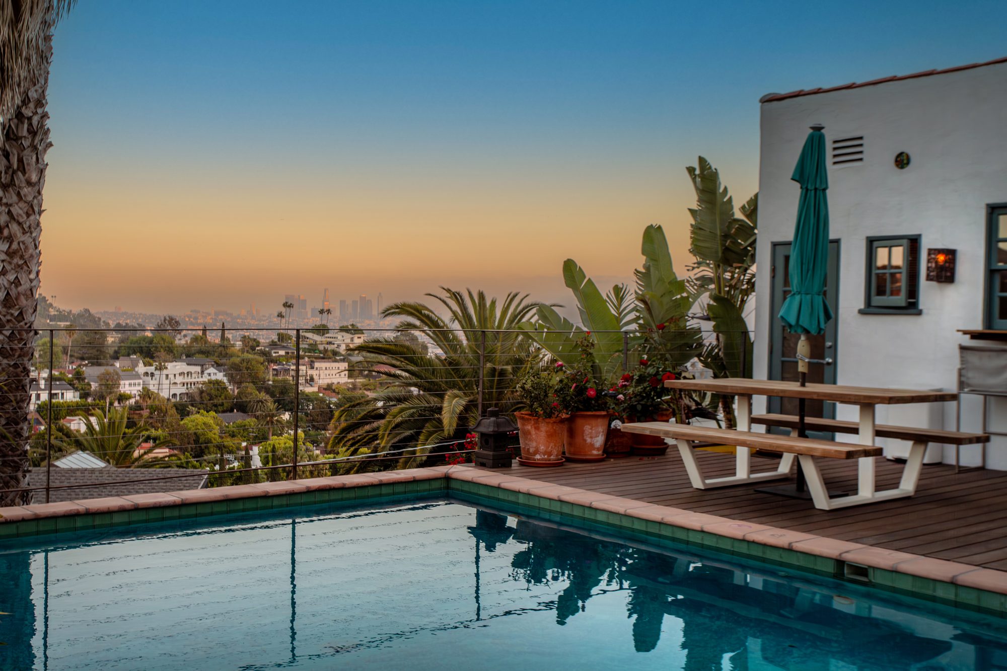 The pool and deck at 2525 Dearborn Drive at dusk, with the downtown Los Angeles skyline on the horizon beyond a cable railing and palms